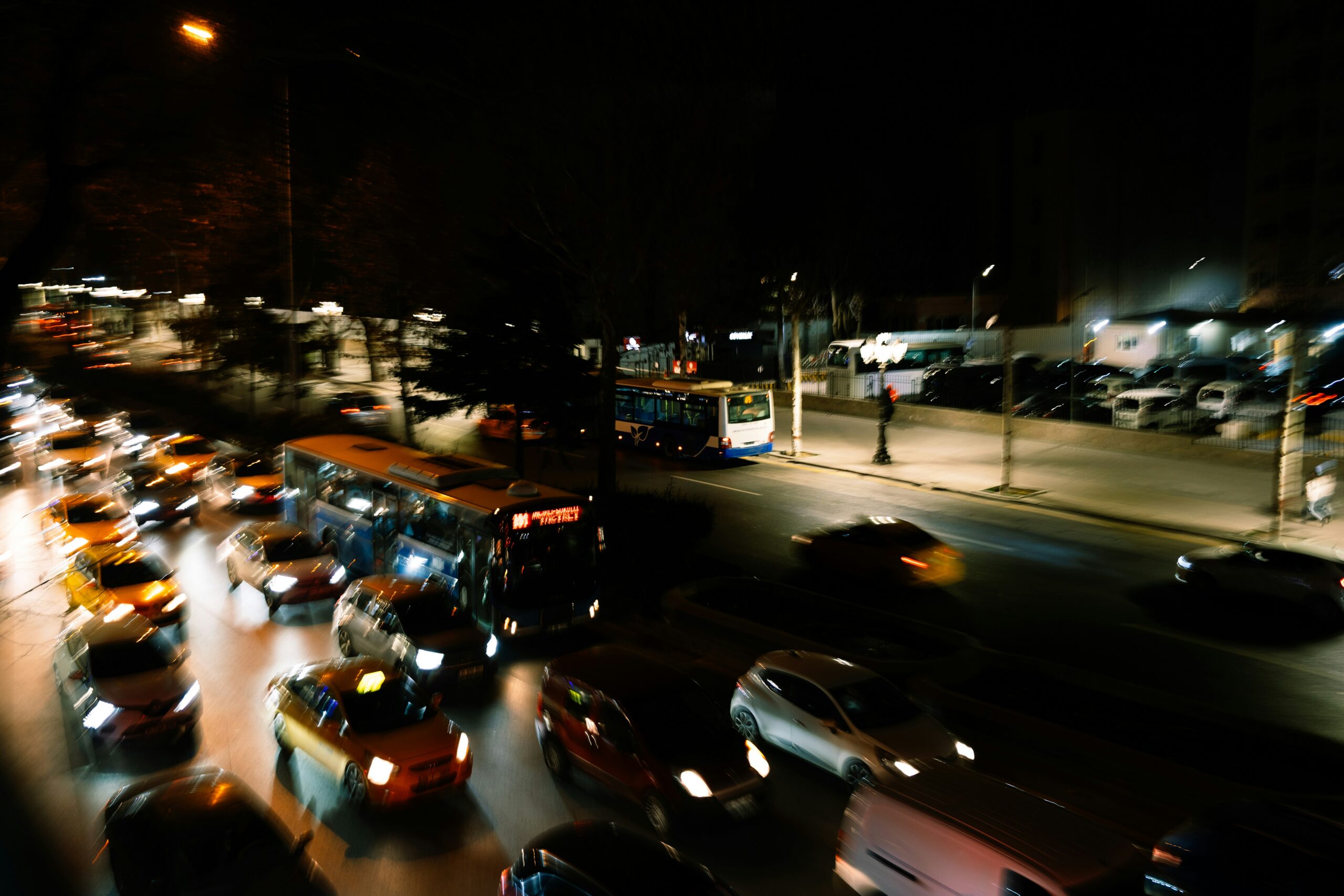 A bustling city street illuminated by neon lights, with cars and pedestrians moving through the vibrant night scene.